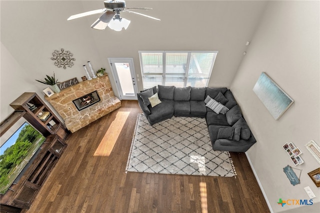 living room with ceiling fan, a stone fireplace, and dark hardwood / wood-style flooring