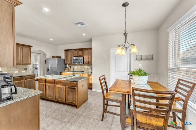 kitchen with light stone counters, a center island, decorative backsplash, appliances with stainless steel finishes, and decorative light fixtures