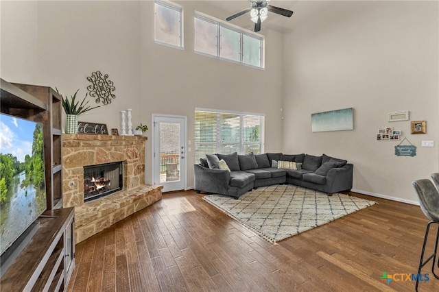 living room with dark wood-type flooring, a towering ceiling, ceiling fan, and a fireplace