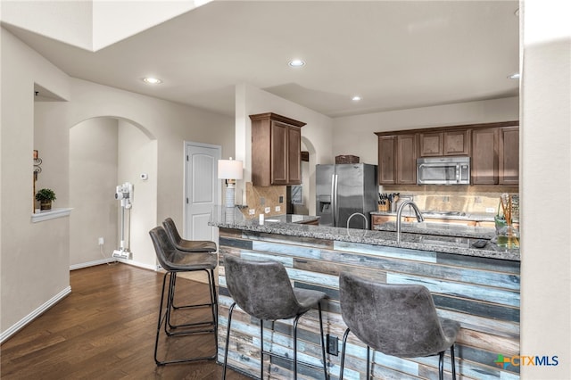 kitchen with dark wood-type flooring, stone countertops, appliances with stainless steel finishes, and tasteful backsplash