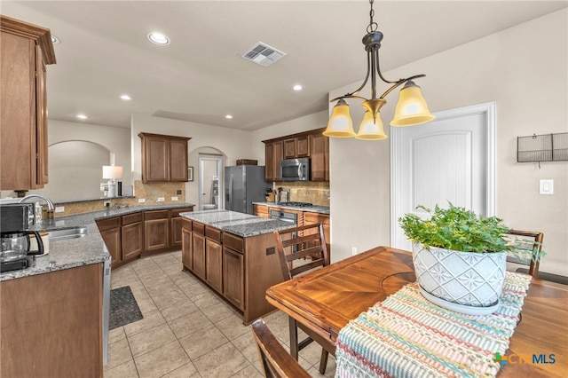 kitchen with decorative backsplash, a kitchen island, light stone countertops, appliances with stainless steel finishes, and decorative light fixtures