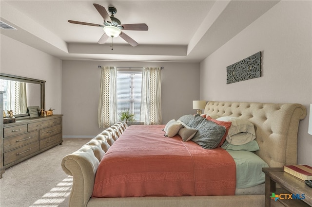 carpeted bedroom with a tray ceiling, multiple windows, and ceiling fan