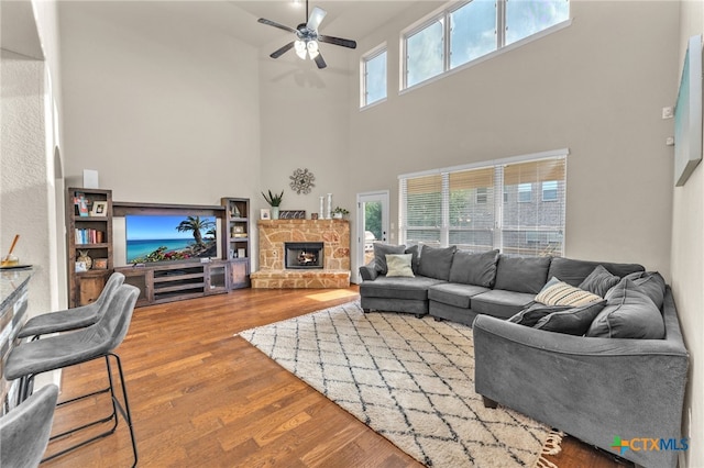 living room featuring a towering ceiling, a fireplace, wood-type flooring, and ceiling fan