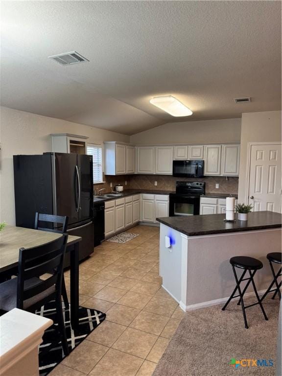 kitchen with dark countertops, black appliances, visible vents, and a sink