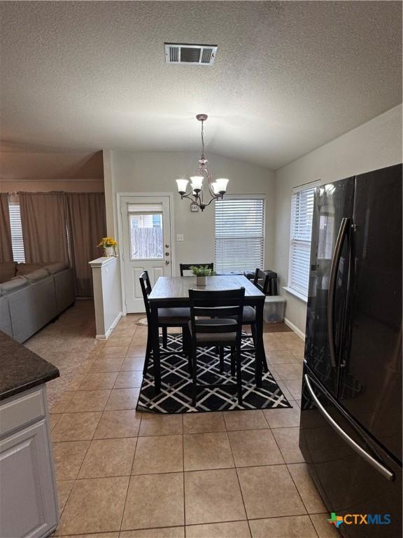 dining area featuring lofted ceiling, a textured ceiling, light tile patterned flooring, and visible vents