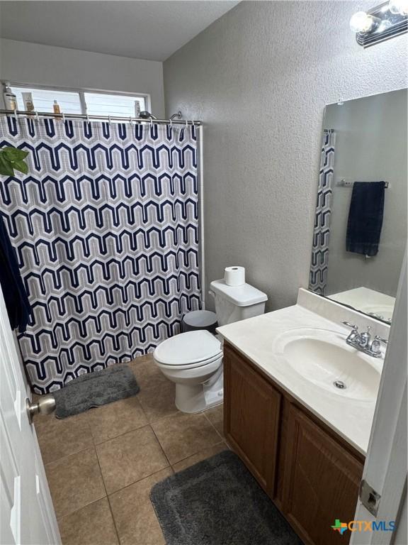 full bathroom featuring curtained shower, a textured wall, toilet, vanity, and tile patterned flooring