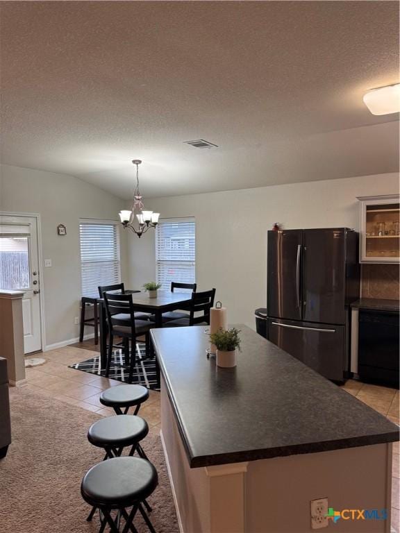 kitchen with lofted ceiling, dark countertops, visible vents, freestanding refrigerator, and a textured ceiling