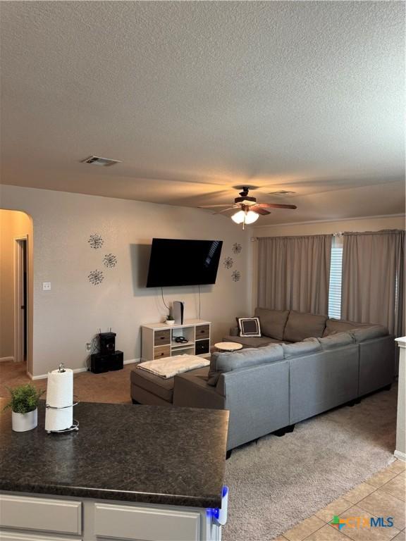 living room featuring arched walkways, visible vents, ceiling fan, and a textured ceiling