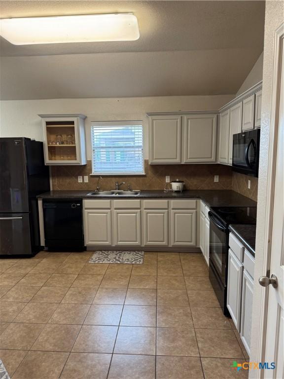 kitchen featuring light tile patterned floors, a sink, black appliances, tasteful backsplash, and dark countertops