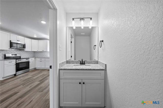 614 S 24th St, Temple, TX 76501 - bathroom featuring a textured wall, tasteful backsplash, wood finished floors, and vanity