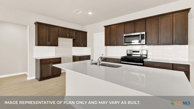 193 Zane Saddle Rd, Lockhart, TX 78644 - kitchen with dark brown cabinetry, a sink, appliances with stainless steel finishes, a center island with sink, and light wood-type flooring