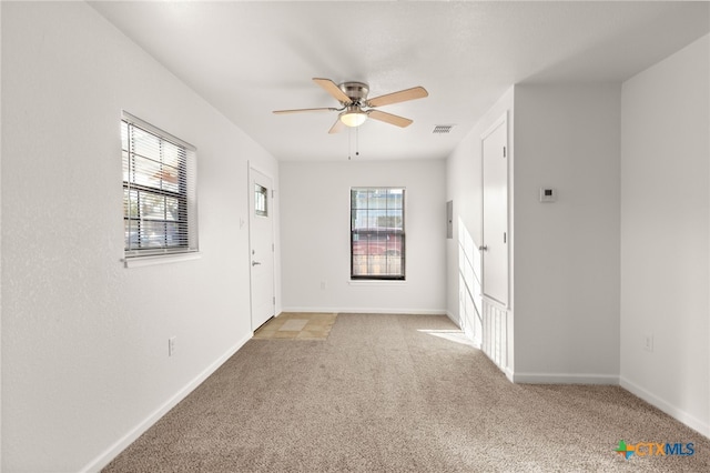 unfurnished room with light carpet, visible vents, baseboards, and ceiling fan