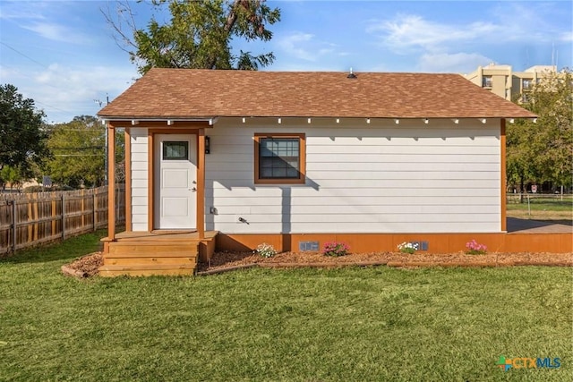 back of property with a lawn, a shingled roof, and fence