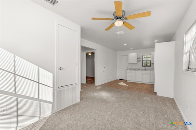 unfurnished living room with a sink, visible vents, light colored carpet, and ceiling fan