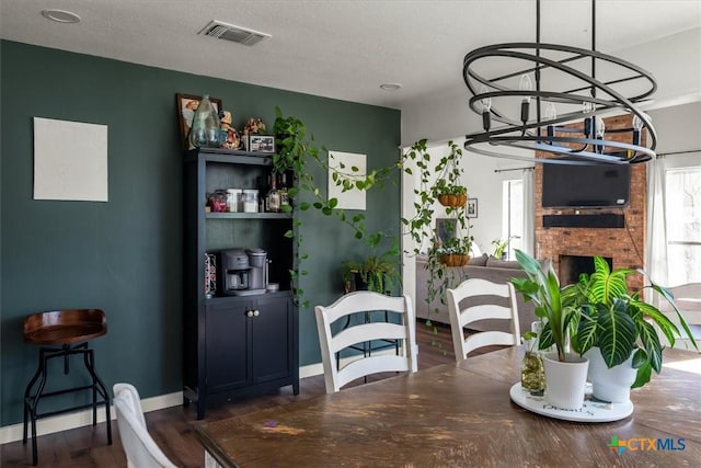 dining area with dark hardwood / wood-style floors, an inviting chandelier, and a fireplace