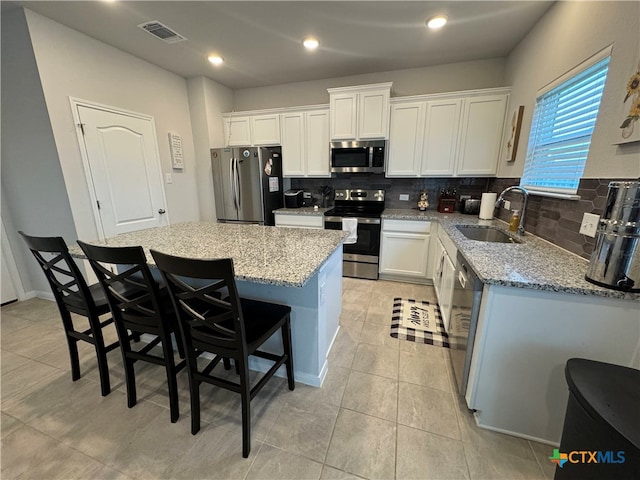 kitchen with white cabinets, sink, a kitchen island, a breakfast bar, and appliances with stainless steel finishes