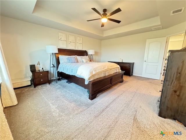 carpeted bedroom with ceiling fan and a tray ceiling