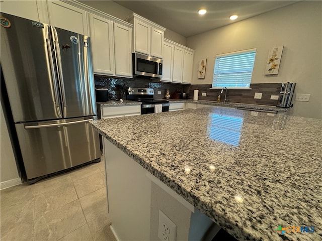 kitchen with stainless steel appliances, white cabinets, light tile patterned floors, backsplash, and light stone countertops