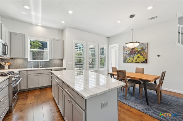 13900 Zink Bnd Unit 61, Austin, TX 78717 - kitchen with gray cabinets, appliances with stainless steel finishes, tasteful backsplash, a kitchen island, and dark wood-style floors