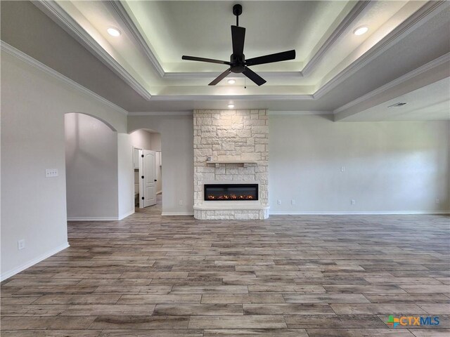 719 Eagle Claw Dr, Salado, TX 76571 - unfurnished living room featuring a raised ceiling, a ceiling fan, arched walkways, wood finished floors, and crown molding