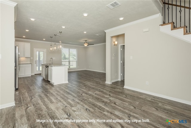 kitchen featuring wood-type flooring, appliances with stainless steel finishes, decorative light fixtures, white cabinets, and a kitchen island with sink