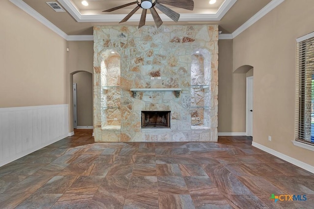 unfurnished living room with crown molding, a raised ceiling, arched walkways, visible vents, and a ceiling fan