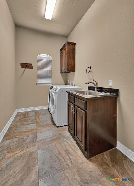 washroom with independent washer and dryer, baseboards, a textured ceiling, a sink, and cabinet space