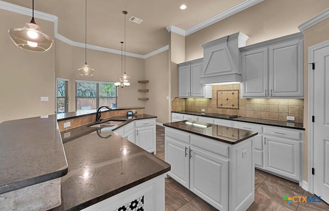 kitchen featuring a large island with sink, premium range hood, decorative backsplash, a sink, and visible vents
