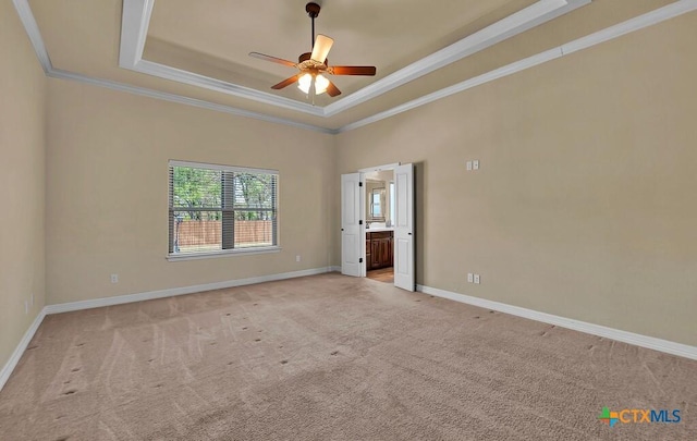 spare room with a tray ceiling, a ceiling fan, light carpet, baseboards, and ornamental molding