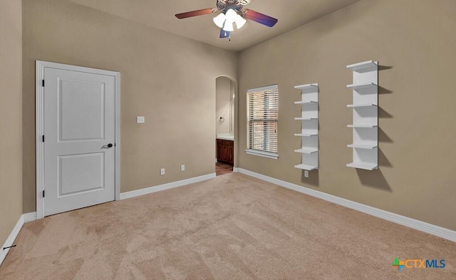 unfurnished bedroom with baseboards, ensuite bath, arched walkways, and light colored carpet