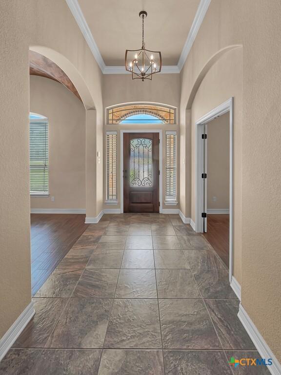 foyer with an inviting chandelier, ornamental molding, baseboards, and arched walkways