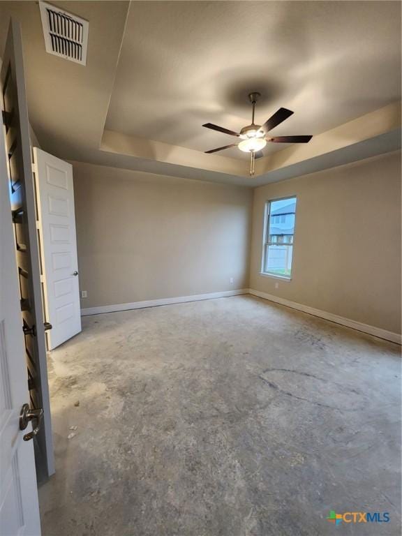 spare room featuring ceiling fan, concrete flooring, and a tray ceiling