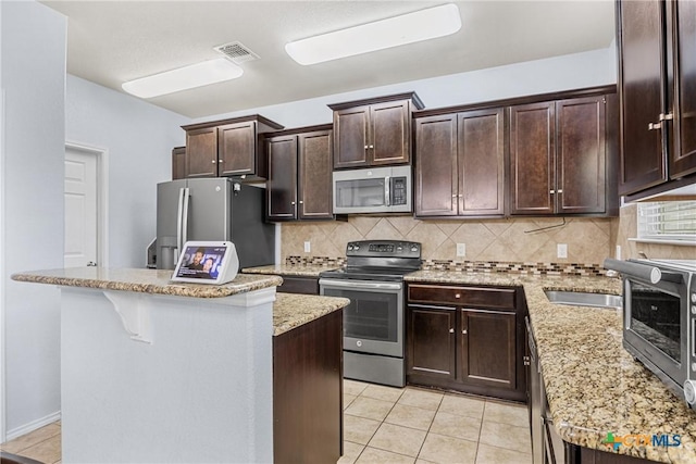 5920 Stonehaven Dr, Temple, TX 76502 - kitchen with stainless steel appliances, light tile patterned floors, dark brown cabinetry, backsplash, and a center island