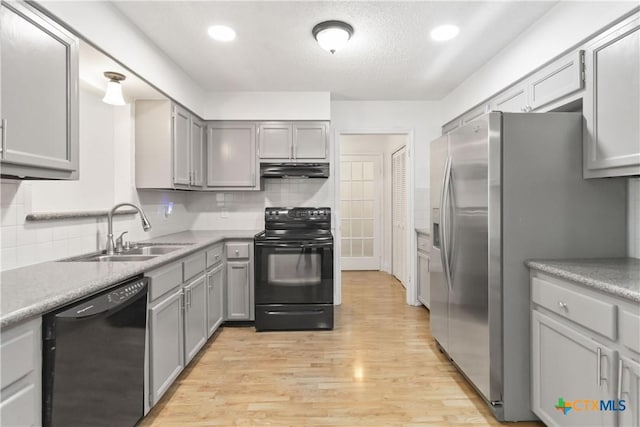 kitchen with sink, light hardwood / wood-style flooring, gray cabinets, backsplash, and black appliances