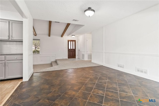 unfurnished living room featuring beam ceiling, dark tile patterned floors, and a textured ceiling