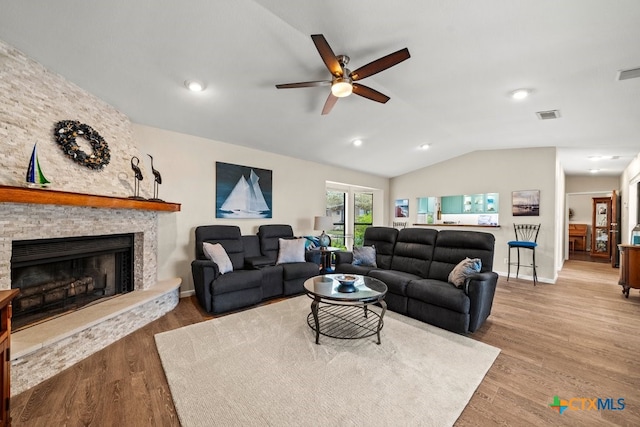 living room with vaulted ceiling, ceiling fan, light hardwood / wood-style flooring, and a stone fireplace