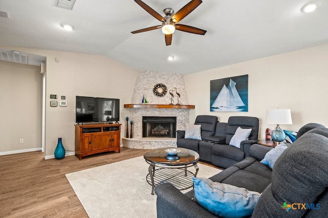 living room with hardwood / wood-style flooring, ceiling fan, a stone fireplace, and lofted ceiling