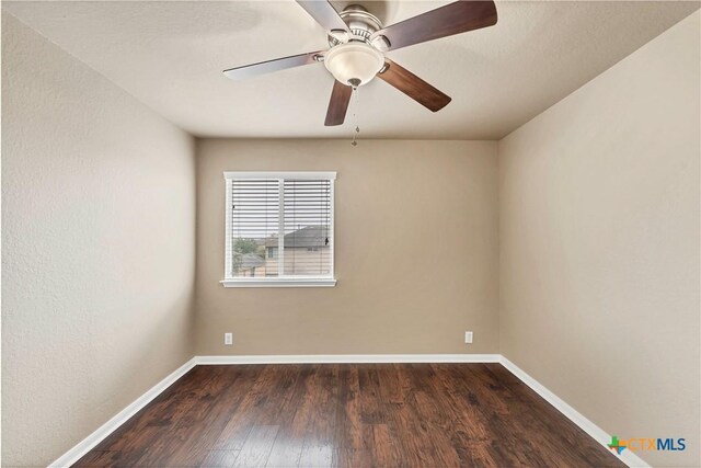 spare room featuring dark wood-style floors, a ceiling fan, and baseboards