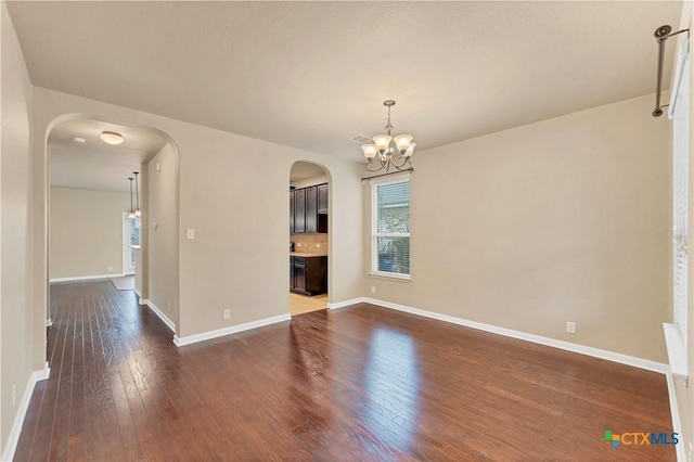 unfurnished room featuring arched walkways, dark wood finished floors, baseboards, and an inviting chandelier