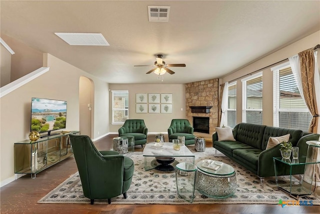 living area featuring visible vents, a ceiling fan, arched walkways, a stone fireplace, and baseboards