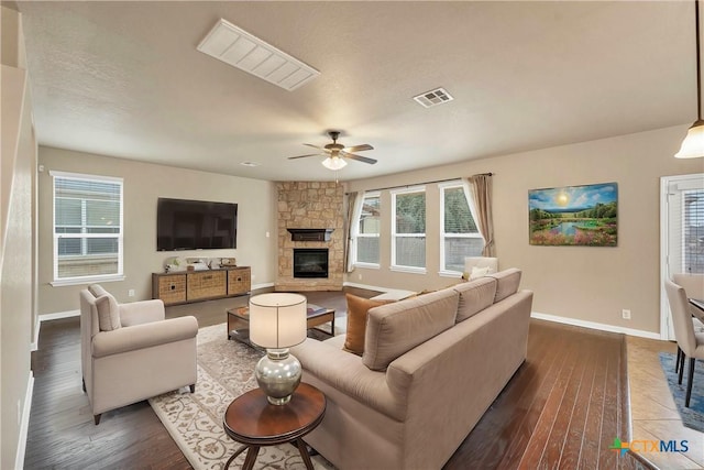 living room with dark wood-style floors, visible vents, plenty of natural light, and a stone fireplace