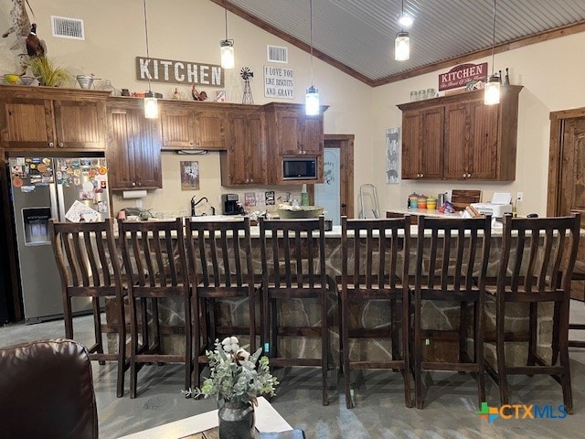 kitchen featuring built in microwave, high vaulted ceiling, stainless steel refrigerator with ice dispenser, hanging light fixtures, and a breakfast bar