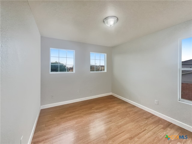 empty room with a textured ceiling and light hardwood / wood-style flooring