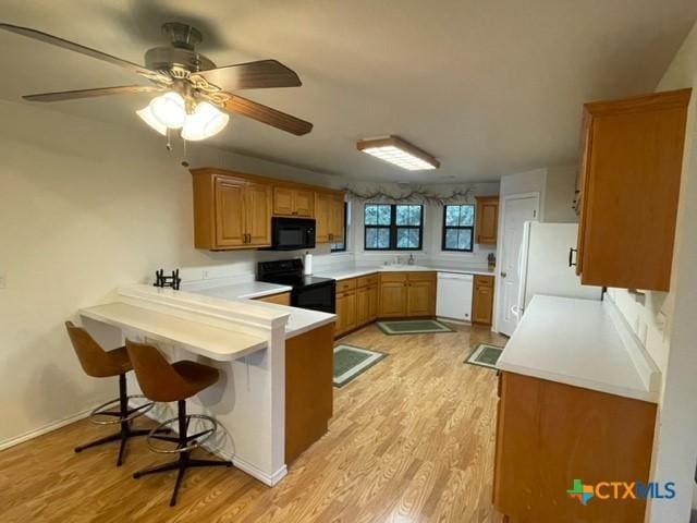 kitchen featuring a breakfast bar area, light wood finished floors, light countertops, white appliances, and a peninsula