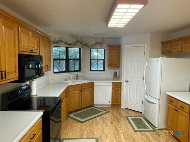 kitchen featuring light wood-type flooring, black appliances, light countertops, and a sink