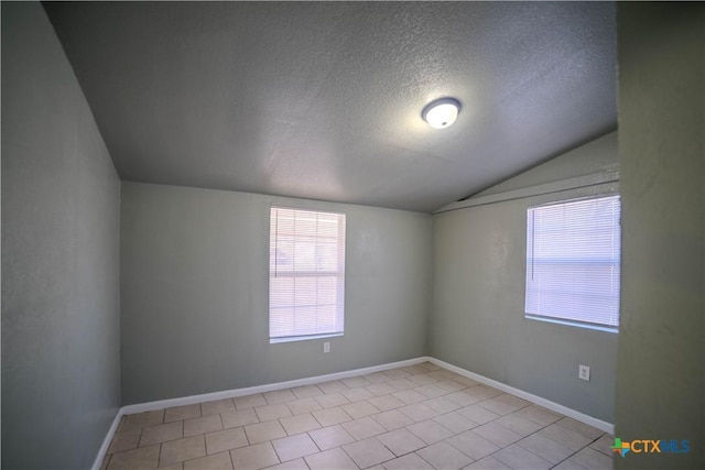 spare room featuring vaulted ceiling, a textured ceiling, and light tile patterned flooring