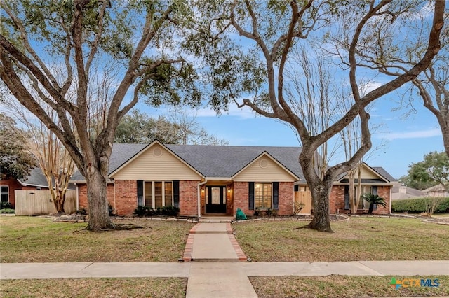 view of front of home featuring a shingled roof, a front yard, and brick siding