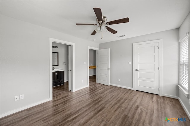 unfurnished bedroom featuring visible vents, a ceiling fan, ensuite bath, wood finished floors, and baseboards