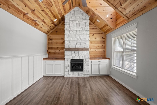 unfurnished living room featuring vaulted ceiling, a stone fireplace, wainscoting, wooden ceiling, and dark wood-style floors