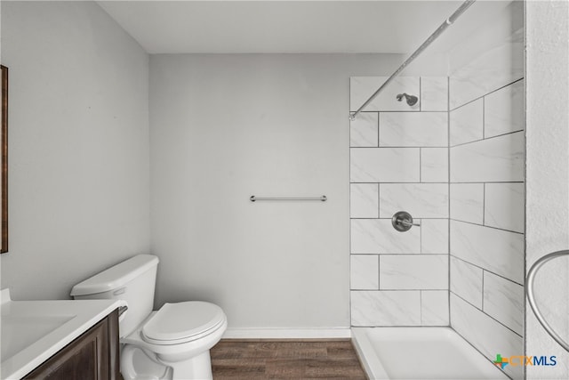 bathroom with baseboards, toilet, a tile shower, wood finished floors, and vanity